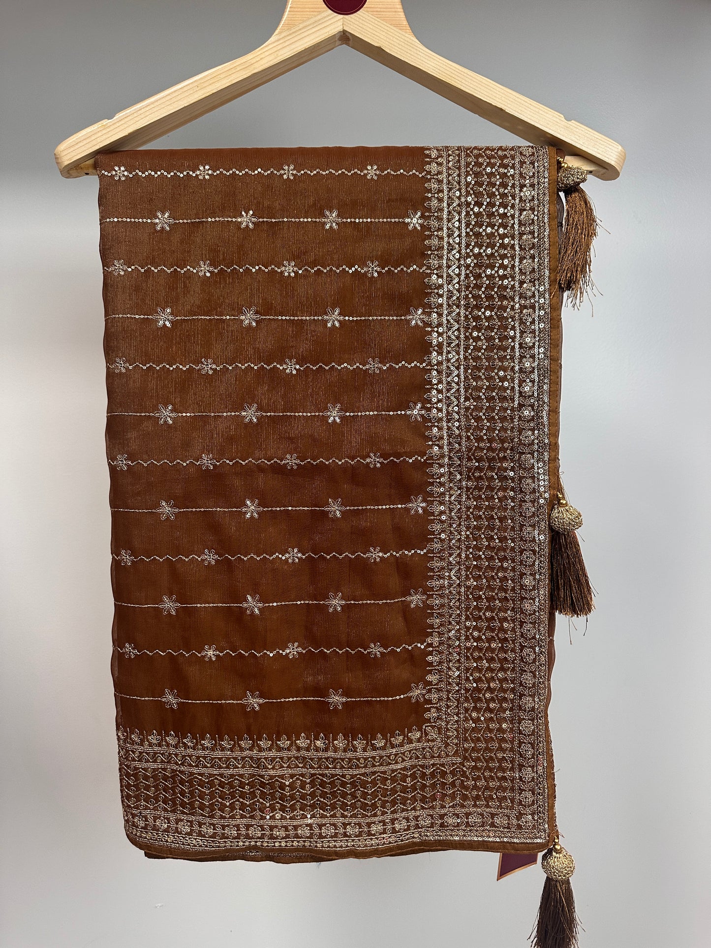 Brown fabric pouch with white embroidery on a wooden hanger against a gray background
