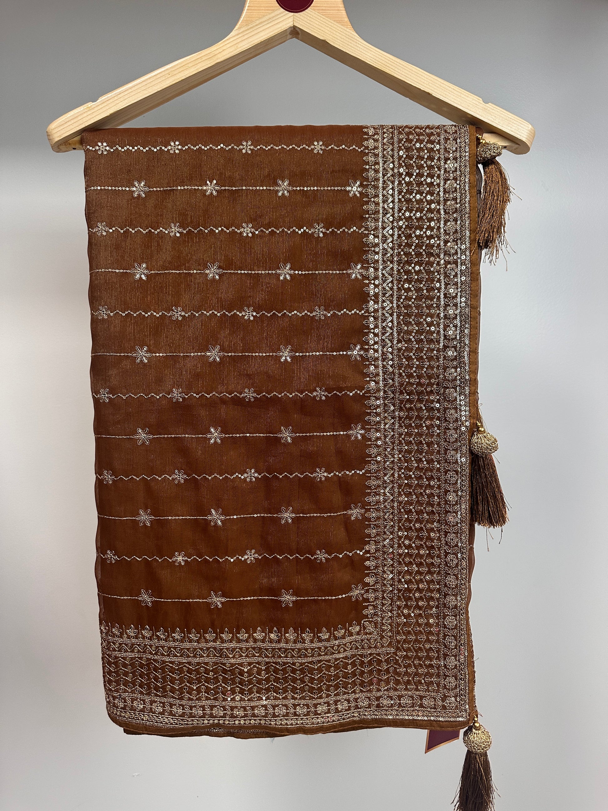 Brown fabric pouch with white embroidery on a wooden hanger against a gray background