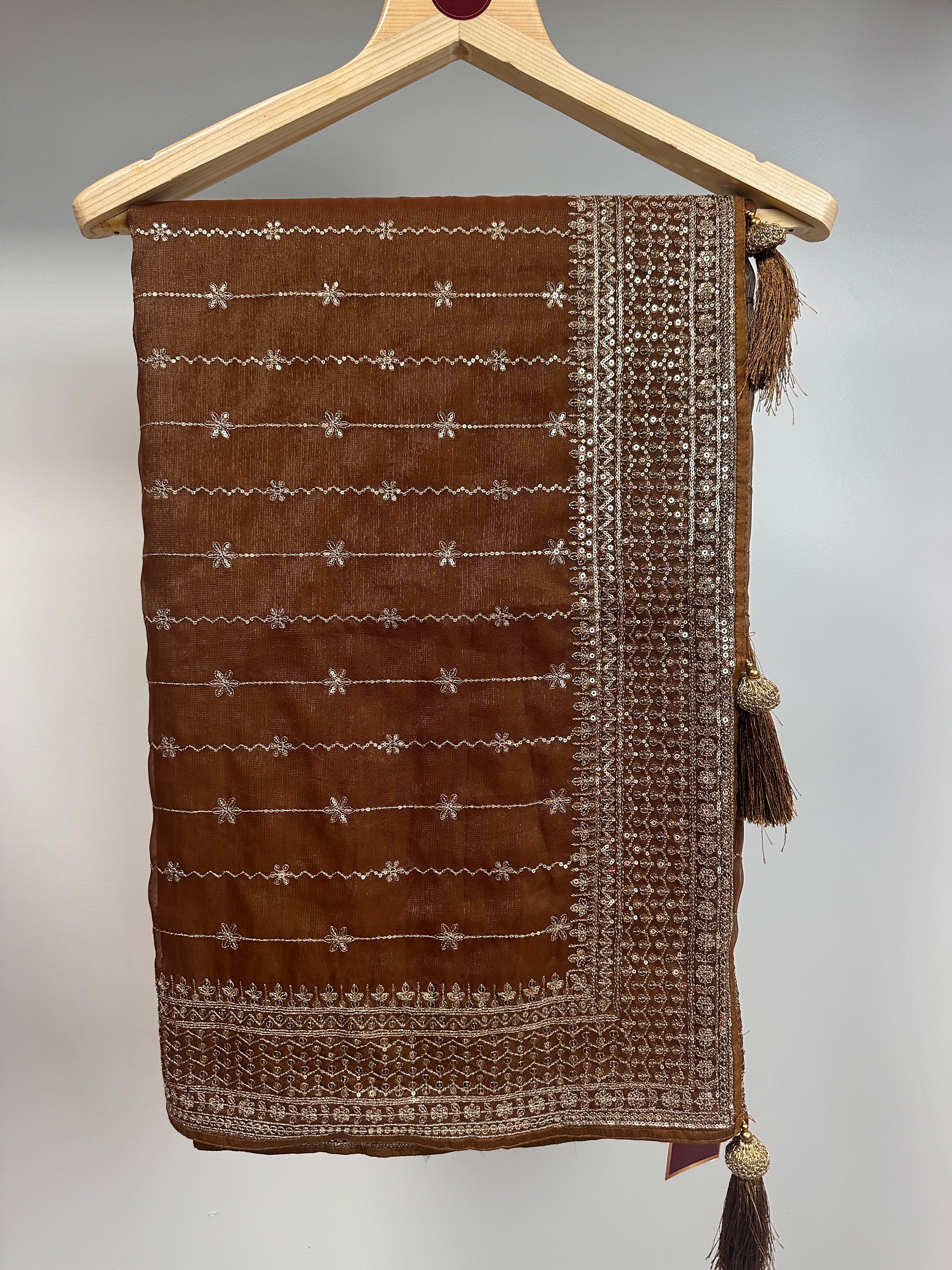 Brown fabric pouch with white embroidery on a wooden hanger against a gray background